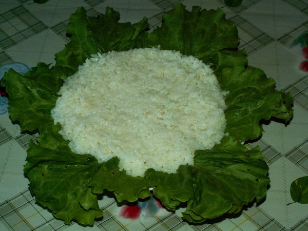 Слой отварного риса на салатных листьях в тарелке