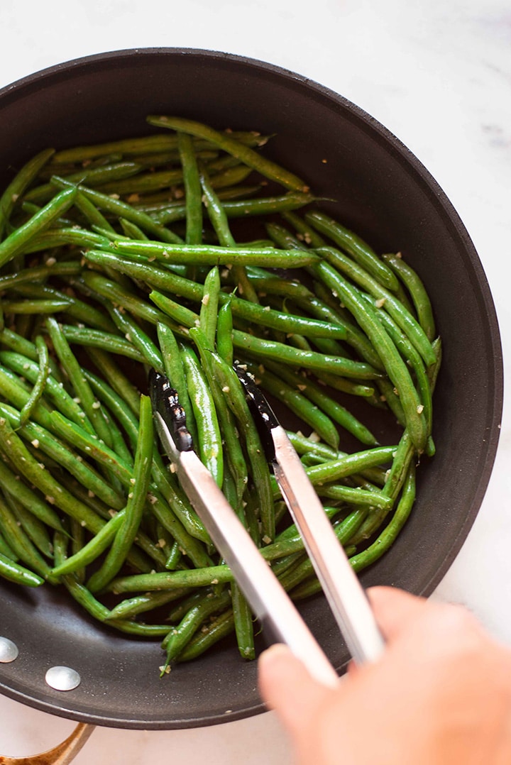 Skillet filled with olive oil, fresh green beans, minced garlic, sea salt, and pepper, sautéing the green beans for the garlic parmesan green beans.