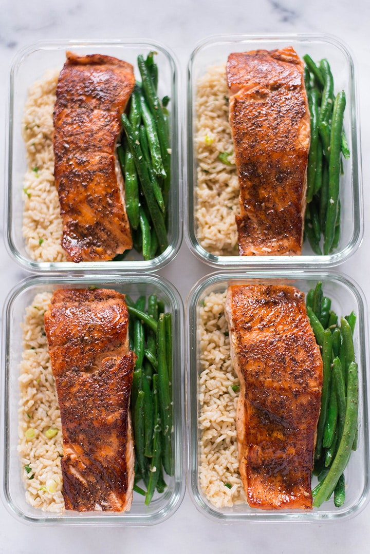 Four meal prep containers, all the same, all filled with garlic rice, garlic parmesan green beans, and pan-roasted salmon for how to meal prep salmon.