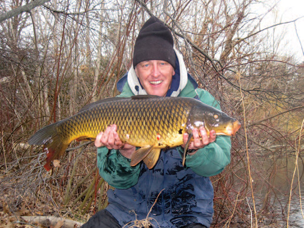 The author holds a common carp of about 14 pounds, taken right after ice out in early March last year. It was caught on sweet corn fished on a hair rig. Carp will begin hitting in shallow ponds as soon as the ice leaves.